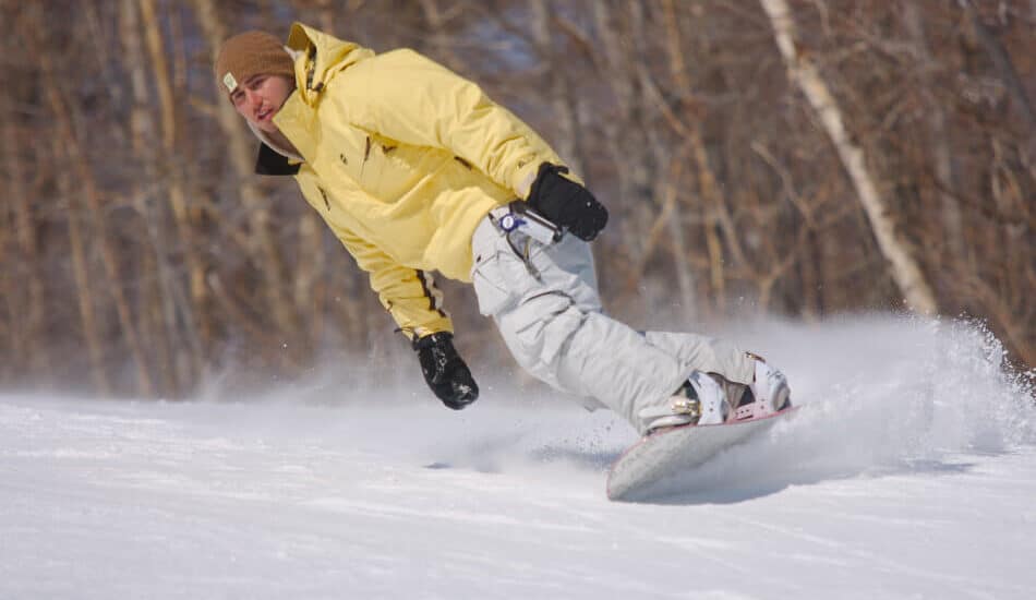 a man with white ski pants and a yellow jacket snowboarding