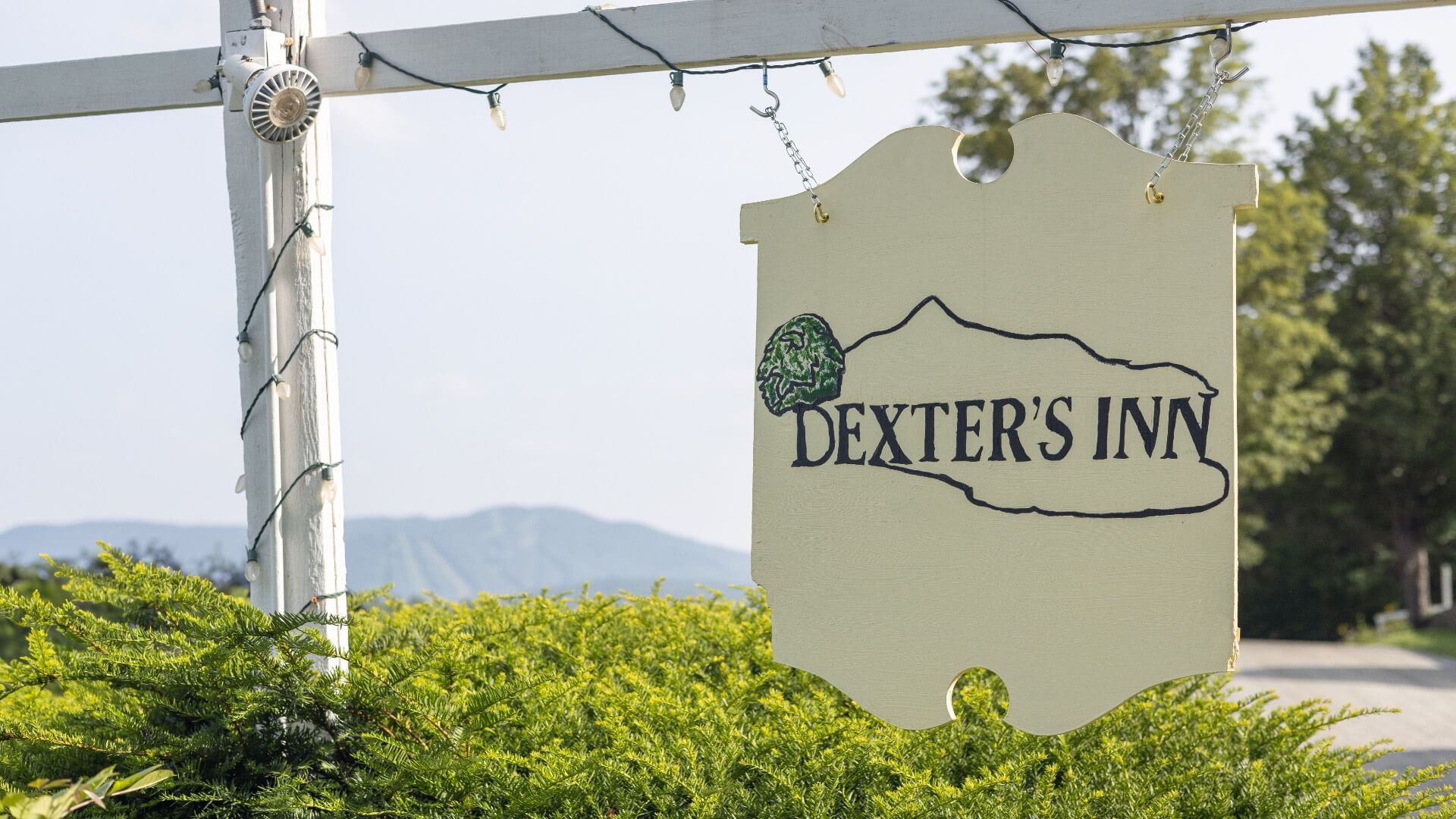 A pale yellow sign that says Dexter's Inn with greenery in front of the side, trees and sweeping mountains in the background.