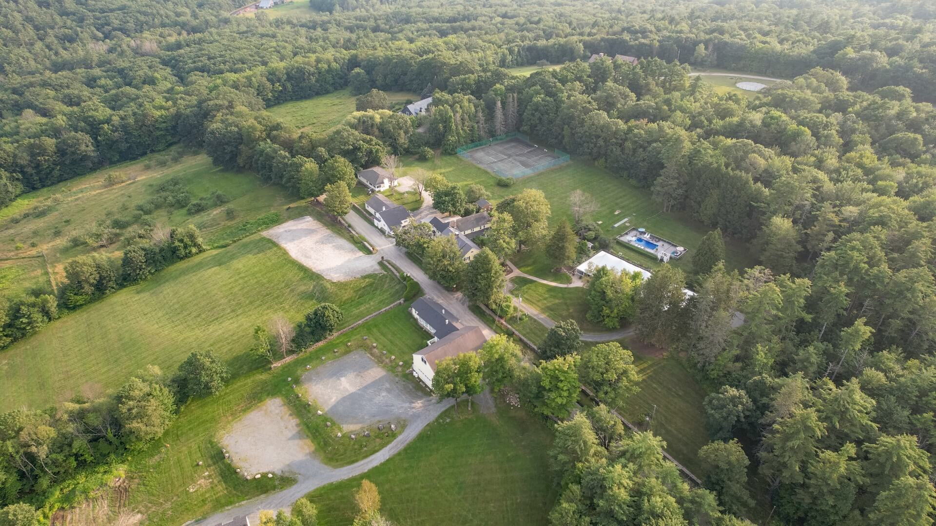 An aerial photo of an estate with a large house, tennis courts, swimming pool, and lots of grounds and outbuildings.