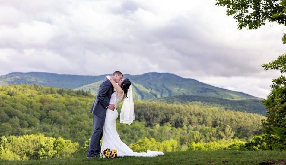 A wedding couple kissing in front of sweeping mountains and lush green hills.